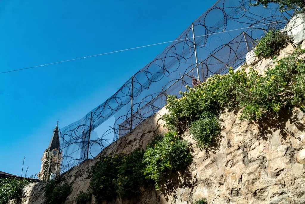 Coils of razor wire above an old stone wall in the Christian Quarter, a church spire against a blue sky, Christian Quarter, Jerusalem